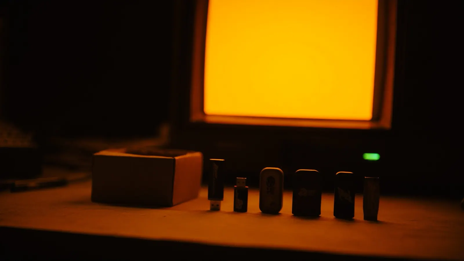 A row of USB flash drives standing in a line in front of a glowing amber monitor
